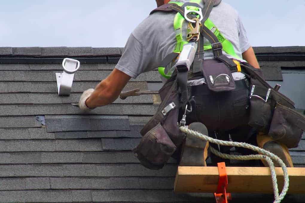 roofer with harness installing roof shingles; how much do roofers make