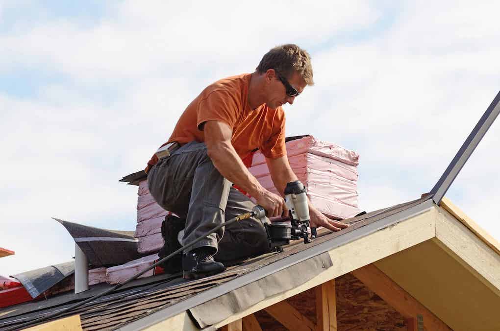 professional roofing contractor nailing down asphalt roof; how much do roofers make?