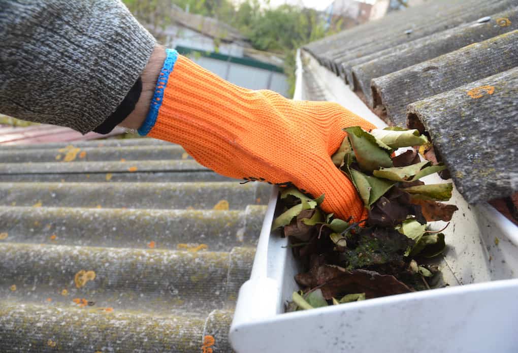 man cleaning gutters; roofing gloves for fall