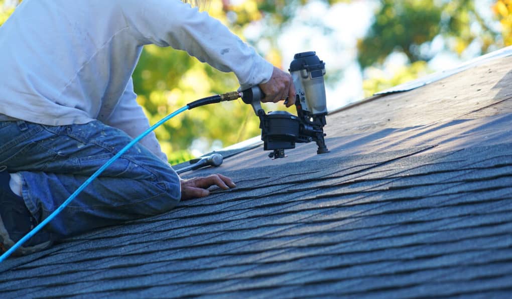 worker installing shingles using a nail gun for a roof warranty